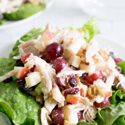 A tabletop view of chicken waldorf salad on a white plate with lettuce and glass of water