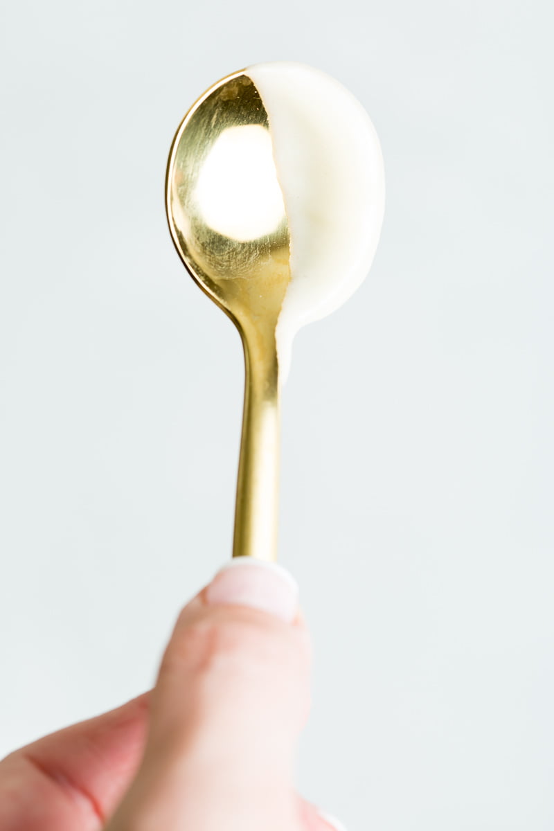 A close up image of a gold spoon covered halfway in thick sweetened condensed milk. 